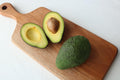 Avocado cut in half on a wooden cutting board with a whole avocado next to it.