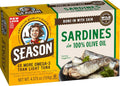 A box of Season brand Sardines in 100% Olive Oil, featuring a yellow and white packaging design with green accents, a cartoon illustration of a man, and a photo of cooked sardines on the front.
