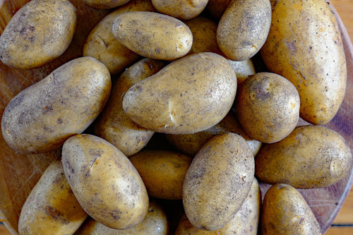 A close-up pile of small brownish-yellow potatoes with rough, speckled skins, filling the frame.