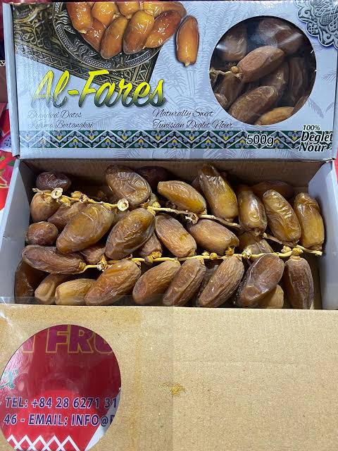 A 1kg open cardboard box of Al-Fares sweet dates, showing rows of brown dates inside alongside a clear window displaying more dates. The top of the box features a decorative label with the brand name 'Al-Fares' and product details.