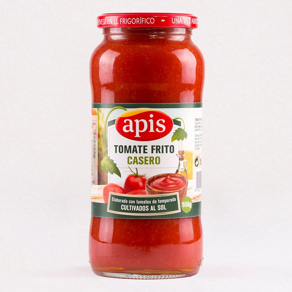A glass jar of apis Tomate Frito Casero tomato sauce, showing the red sauce inside, with a white and green label and a red metal lid, set against a plain white background.