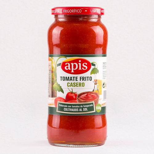 A glass jar of apis Tomate Frito Casero tomato sauce, showing the red sauce inside, with a white and green label and a red metal lid, set against a plain white background.