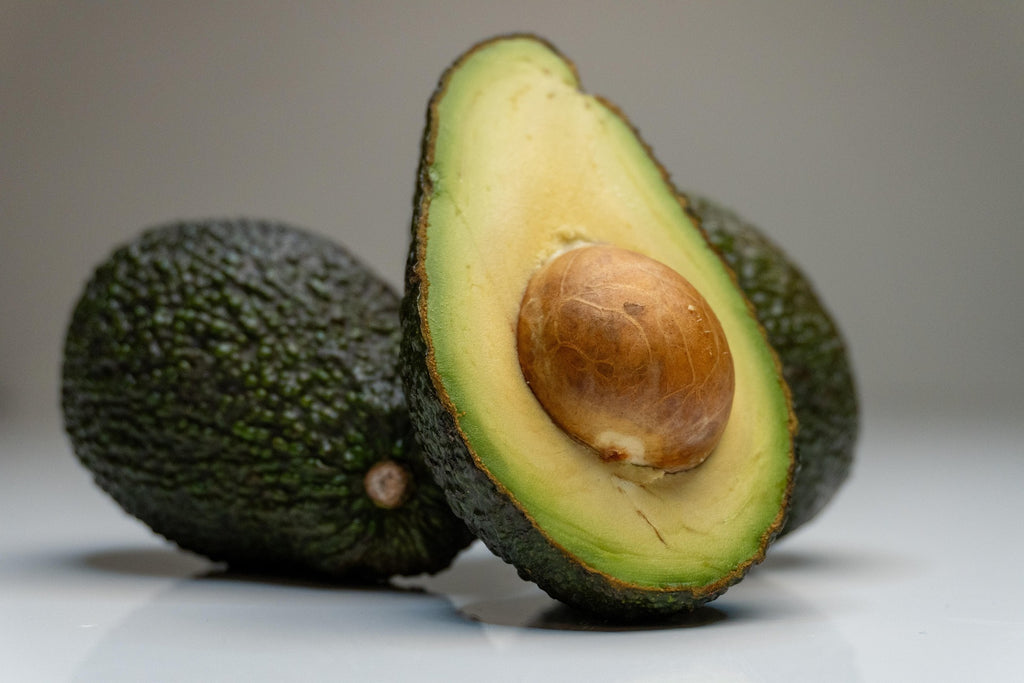 Avocado cut in half with the other whole avocado on a neutral background