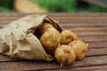 Fresh small potatoes spilling out of a brown paper bag onto a wooden table, with a softly blurred outdoor background.