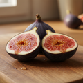 Fresh figs on a wooden cutting board, with one fig whole in the background and two figs cut in half to show the pinkish-red interior and pale rind.