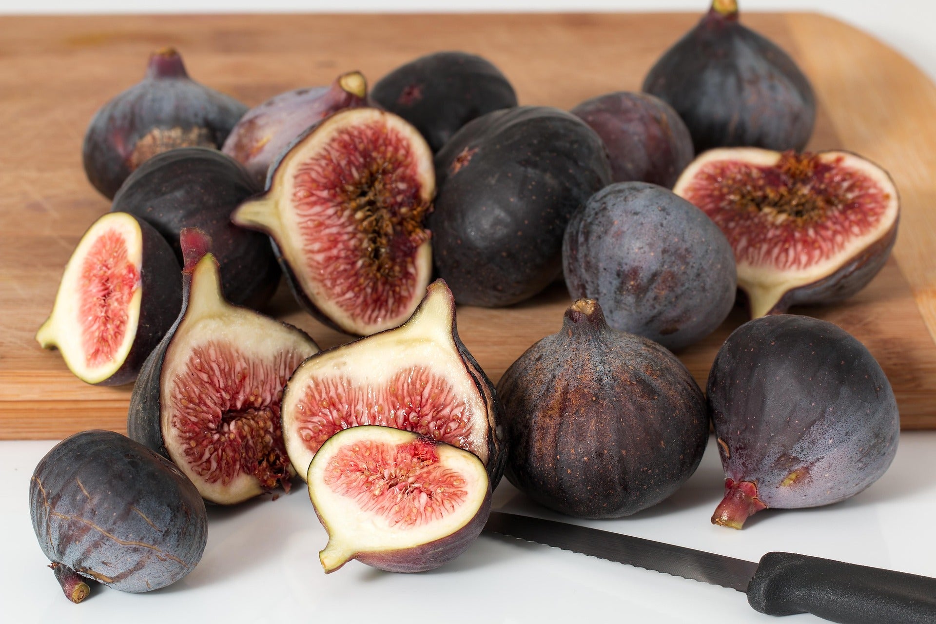 Assorted figs on a wooden cutting board with a knife.