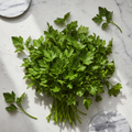 A bunch of fresh green parsley stems and leaves arranged on a white marble surface with a few loose sprigs nearby.