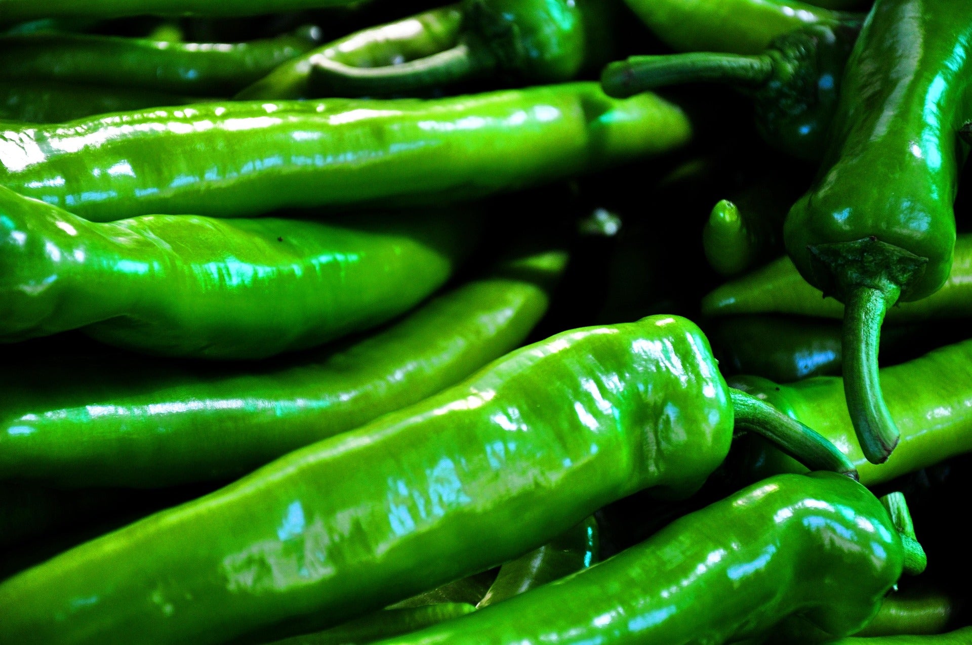 A close-up pile of glossy bright green peppers filling the frame.