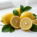 Fresh yellow lemons with green leaves, including whole lemons and two cut halves showing the juicy interior, arranged on a bright white surface near a window.