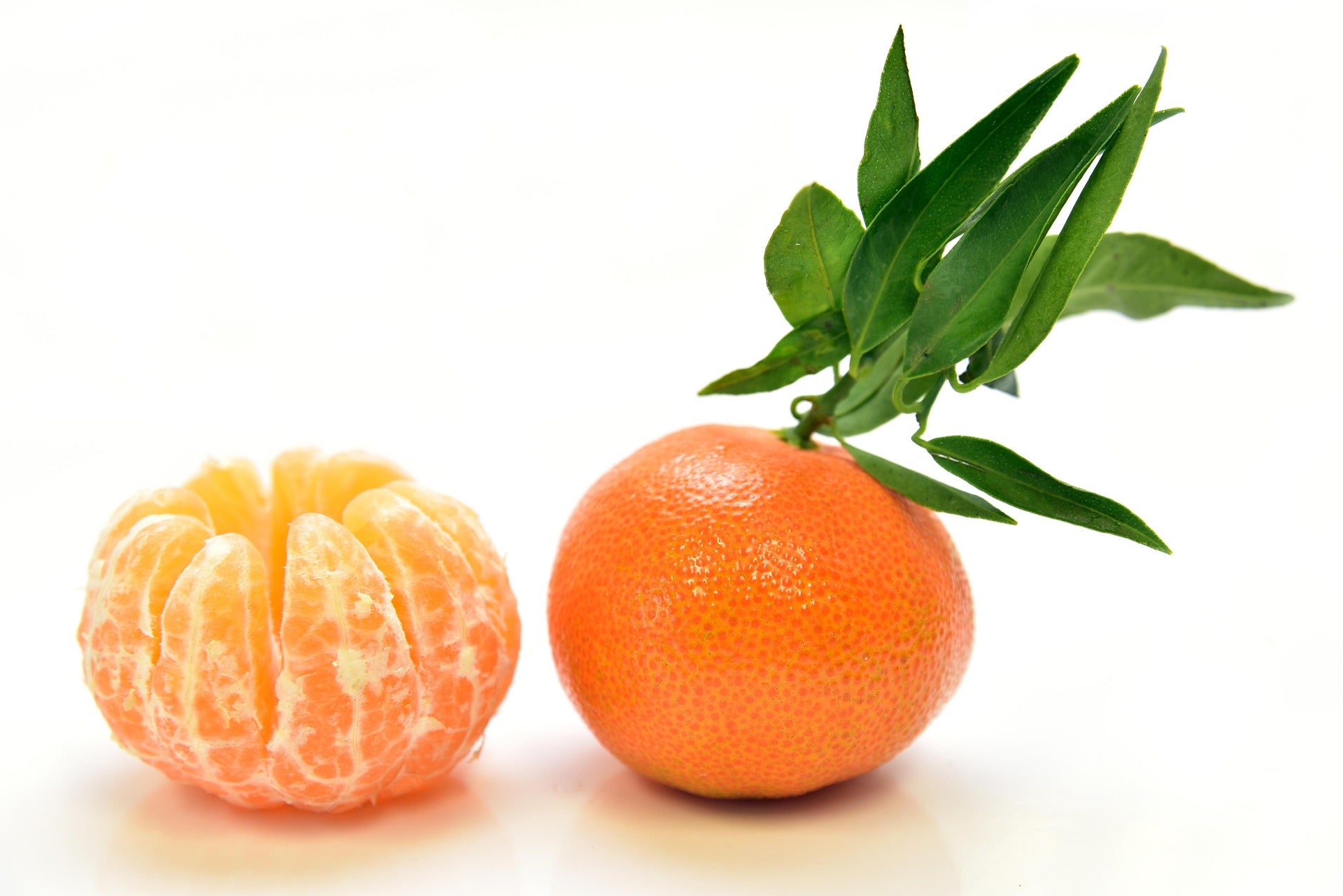 A whole orange with green leaves and a peeled orange segment, photographed on a clean white background.