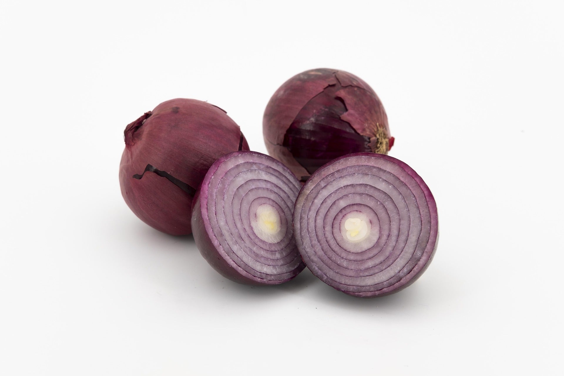 Three red onions on a white background, with two cut in half to show the layered purple-red onion rings and pale centers.