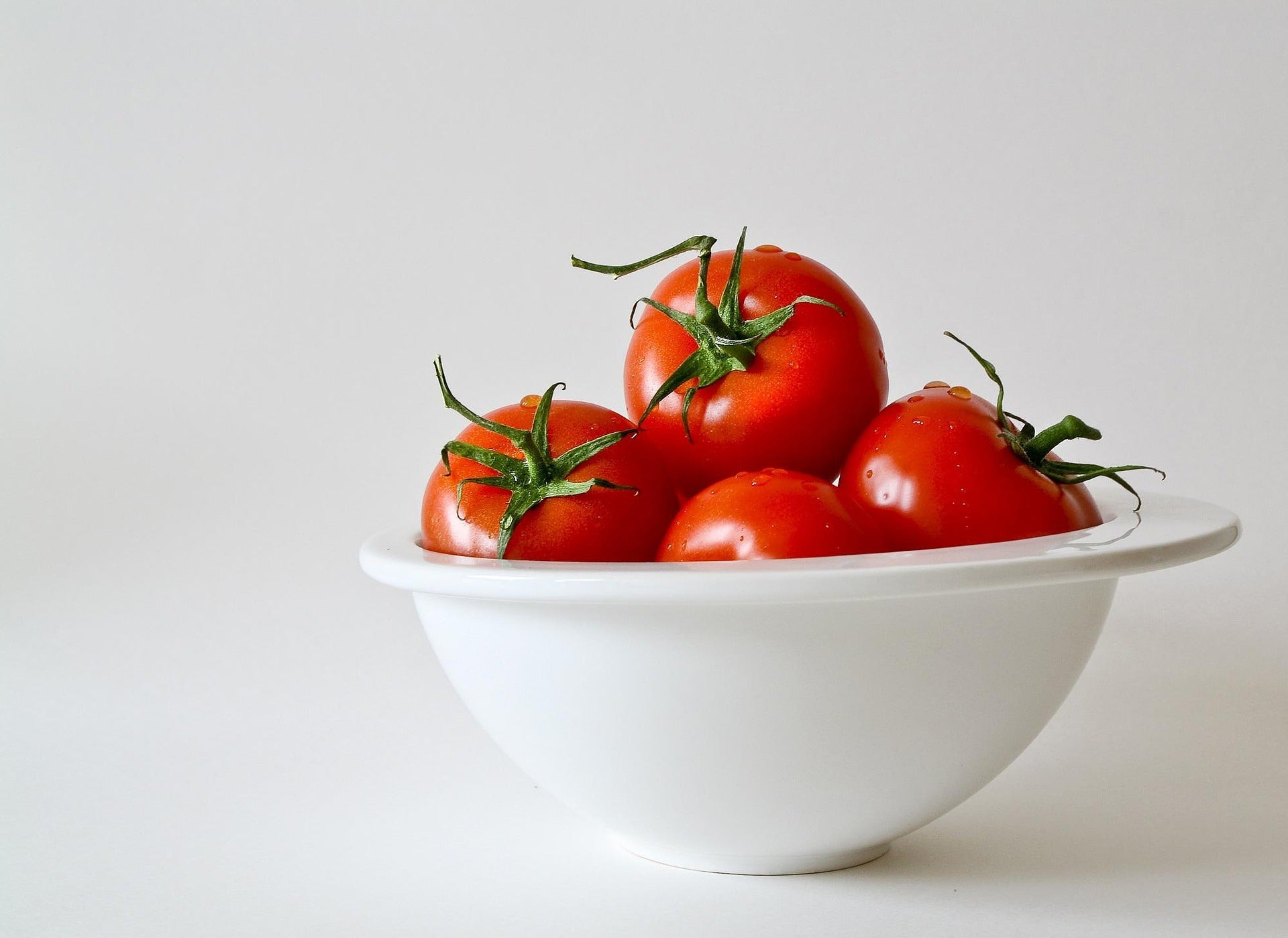 White bowl with red tomatoes on a light gray background